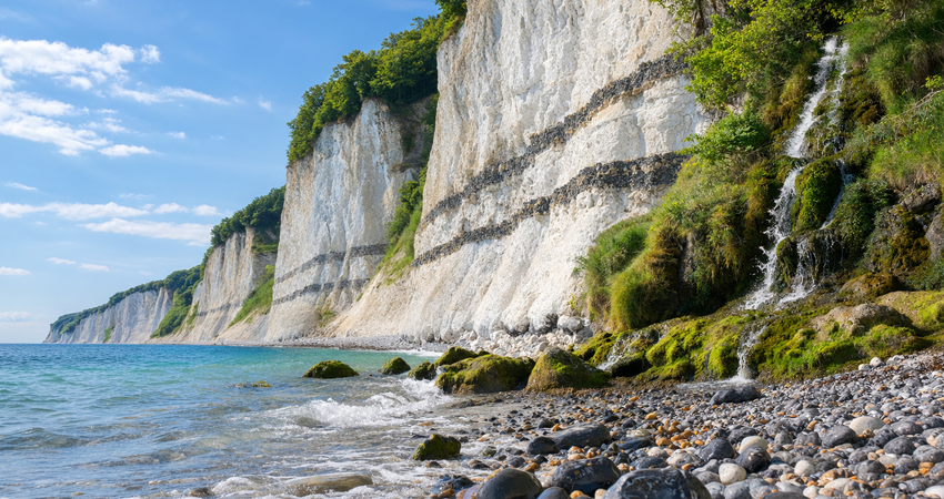 Blick vom Kieselstrand am Kieler Ufer auf die hoch aufragenden weißen Kreidefelsen und den Wasserfall auf Rügen.